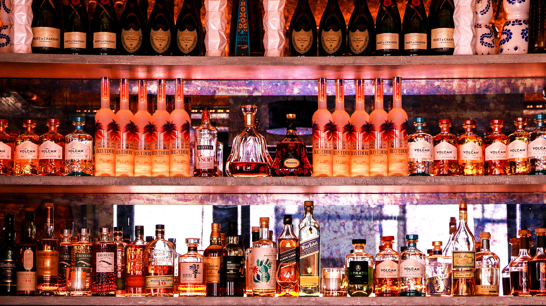 Top-shelf liquor bottles displayed on a backbar shelf inside a nightclub, showcasing premium options for bottle service
