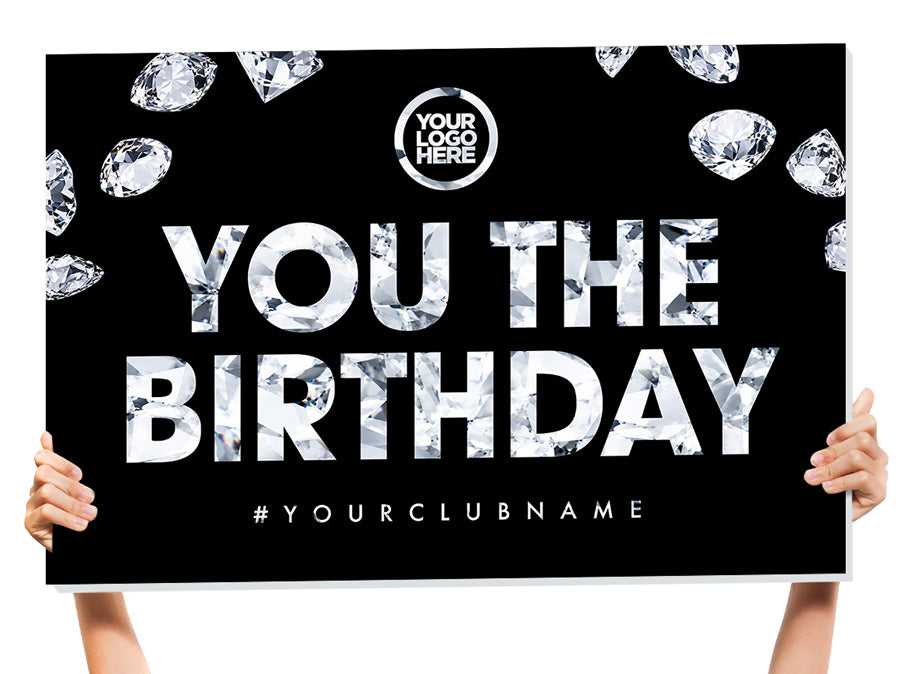 A large black birthday party backdrop banner held up by two people's hands and arms. The banner features a black background decorated with white diamond illustrations, bold white text reading 'YOU THE BIRTHDAY' with a diamond-patterned fill, a circular placeholder logo at the top, and the hashtag '#YOURCLUBNAME' at the bottom.