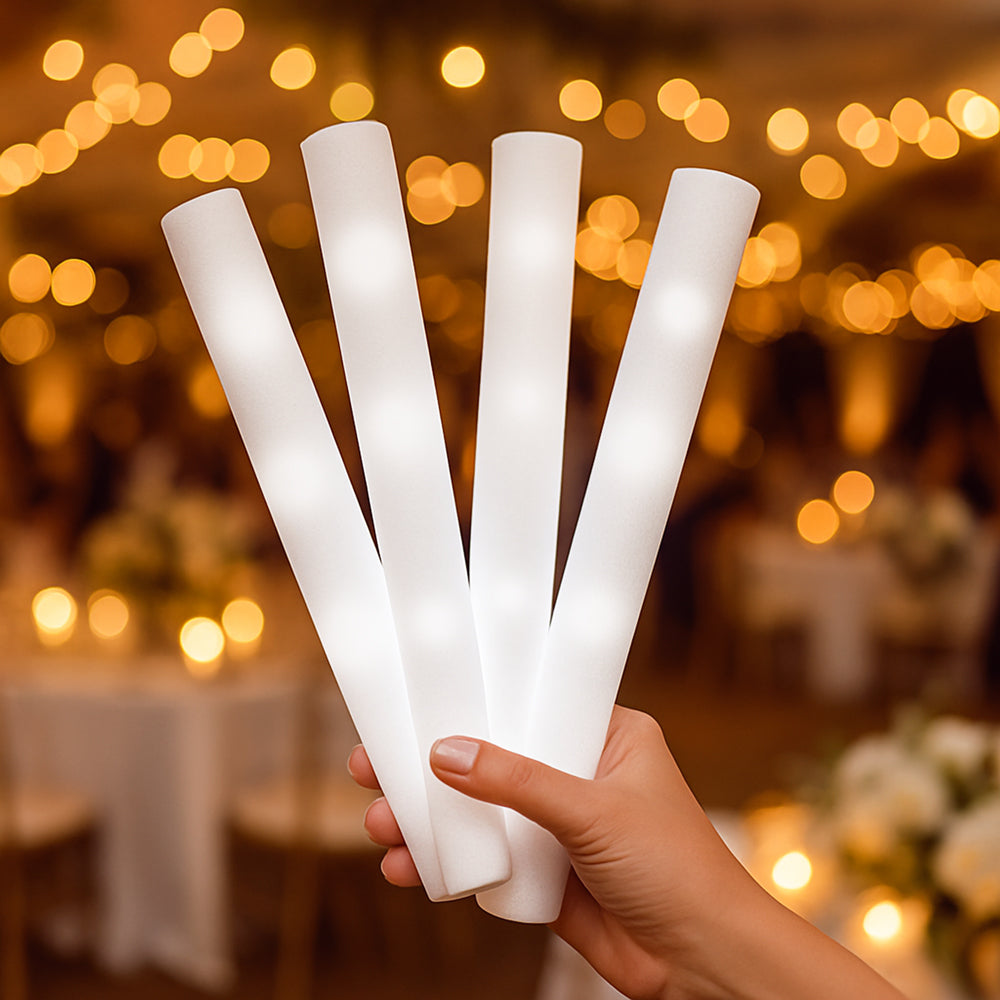 Four white LED foam sticks glowing softly at a wedding reception with warm blurred lights in the background