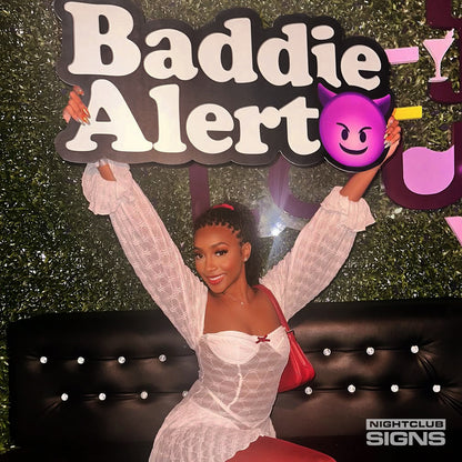 a patron holding up a baddie alert bottle service sign in a nightclub 